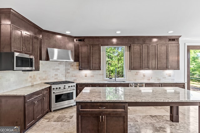 kitchen with a kitchen island, light stone countertops, dark brown cabinetry, sink, and appliances with stainless steel finishes