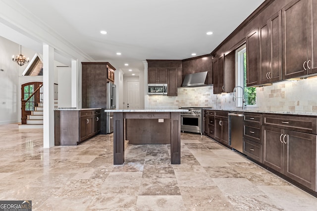 kitchen with light stone counters, dark brown cabinets, wall chimney exhaust hood, appliances with stainless steel finishes, and a center island