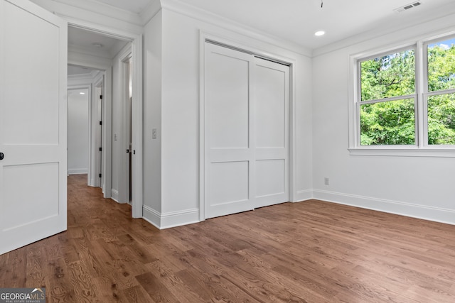 unfurnished bedroom with wood-type flooring, a closet, and crown molding