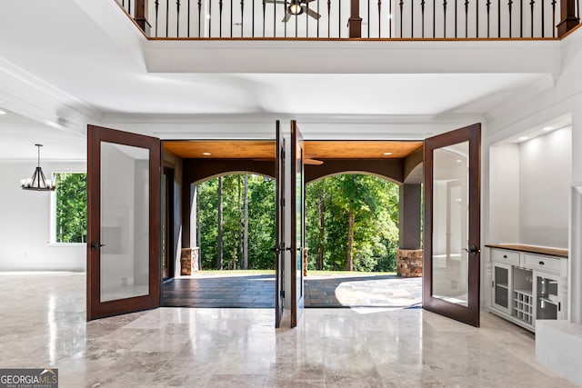 entrance foyer with french doors, a high ceiling, a notable chandelier, and crown molding