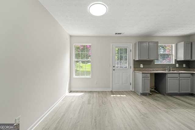 kitchen with sink, gray cabinets, a textured ceiling, and light wood-type flooring