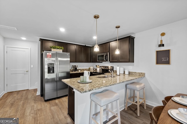 kitchen with sink, stainless steel appliances, light hardwood / wood-style flooring, kitchen peninsula, and decorative light fixtures