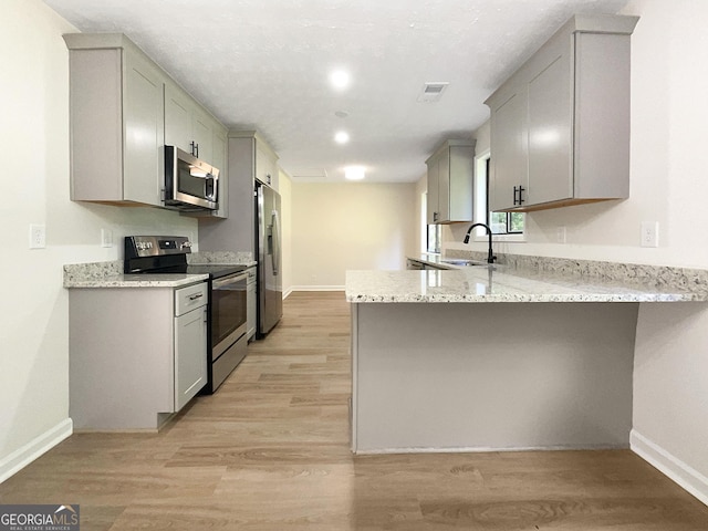 kitchen with kitchen peninsula, appliances with stainless steel finishes, gray cabinetry, sink, and light hardwood / wood-style flooring