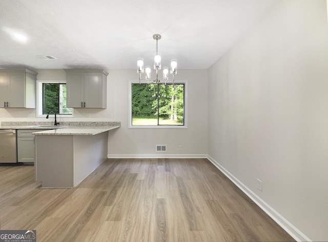 kitchen with stainless steel dishwasher, a healthy amount of sunlight, gray cabinetry, and light wood-type flooring