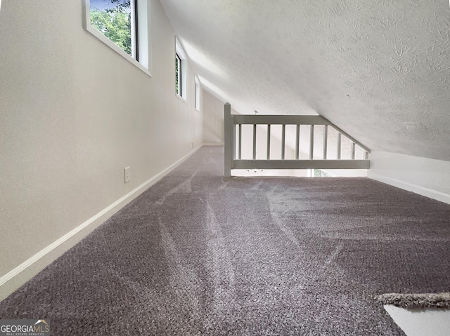 bonus room featuring dark carpet, lofted ceiling, and a textured ceiling