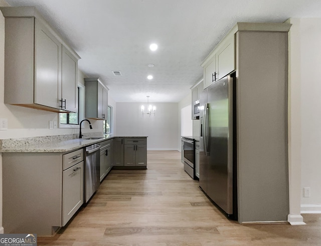 kitchen featuring sink, hanging light fixtures, stainless steel appliances, gray cabinets, and light wood-type flooring