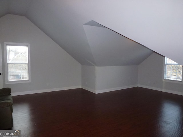 additional living space with dark wood-type flooring, vaulted ceiling, and a healthy amount of sunlight