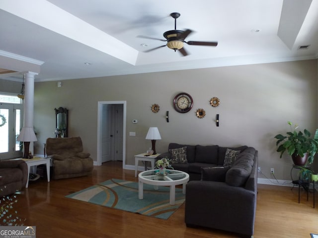 living room featuring wood-type flooring, ceiling fan, a tray ceiling, and ornamental molding