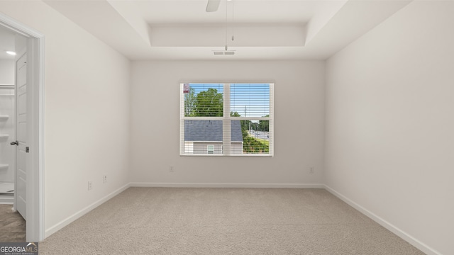 carpeted spare room featuring a raised ceiling and ceiling fan