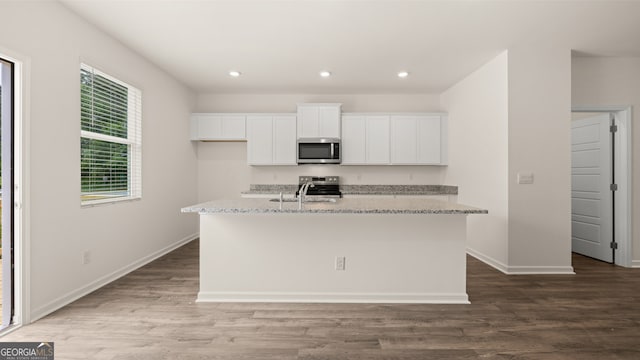 kitchen with appliances with stainless steel finishes, light stone counters, an island with sink, and wood-type flooring