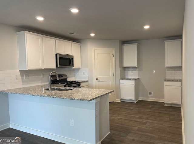 kitchen featuring kitchen peninsula, appliances with stainless steel finishes, light stone counters, dark hardwood / wood-style floors, and white cabinetry