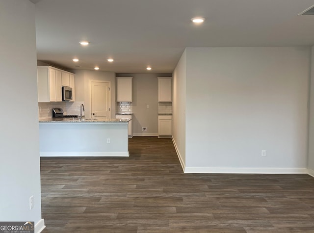 kitchen featuring backsplash, white cabinets, dark hardwood / wood-style floors, light stone countertops, and stainless steel appliances