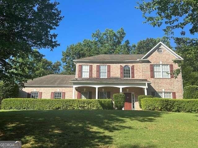 view of front facade featuring covered porch, brick siding, and a front yard