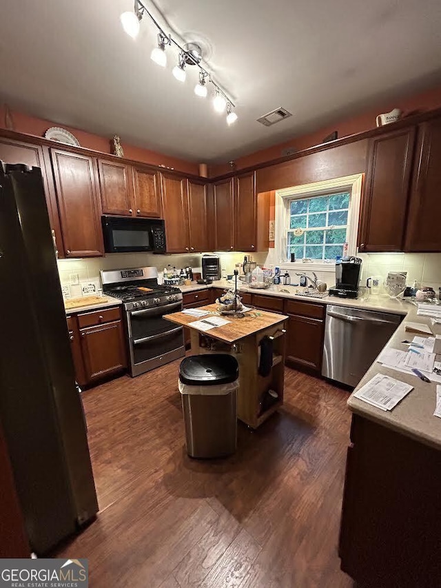 kitchen featuring visible vents, dark wood-type flooring, a center island, stainless steel appliances, and a sink