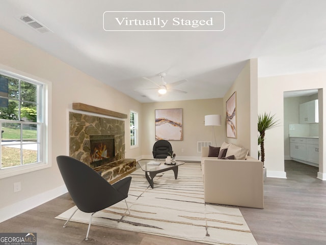 living room featuring hardwood / wood-style floors, a stone fireplace, and ceiling fan