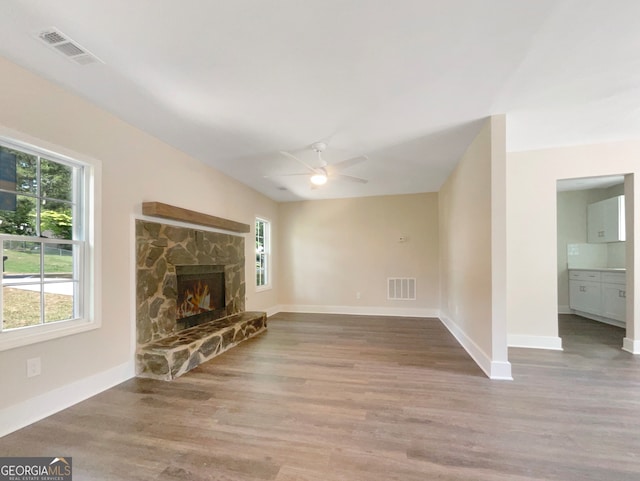 unfurnished living room with a stone fireplace, ceiling fan, and wood-type flooring