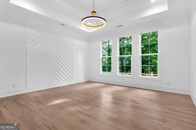 unfurnished room featuring a chandelier, a tray ceiling, and light hardwood / wood-style flooring