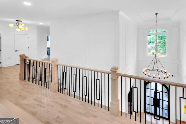 hall featuring light hardwood / wood-style floors, a raised ceiling, and a notable chandelier