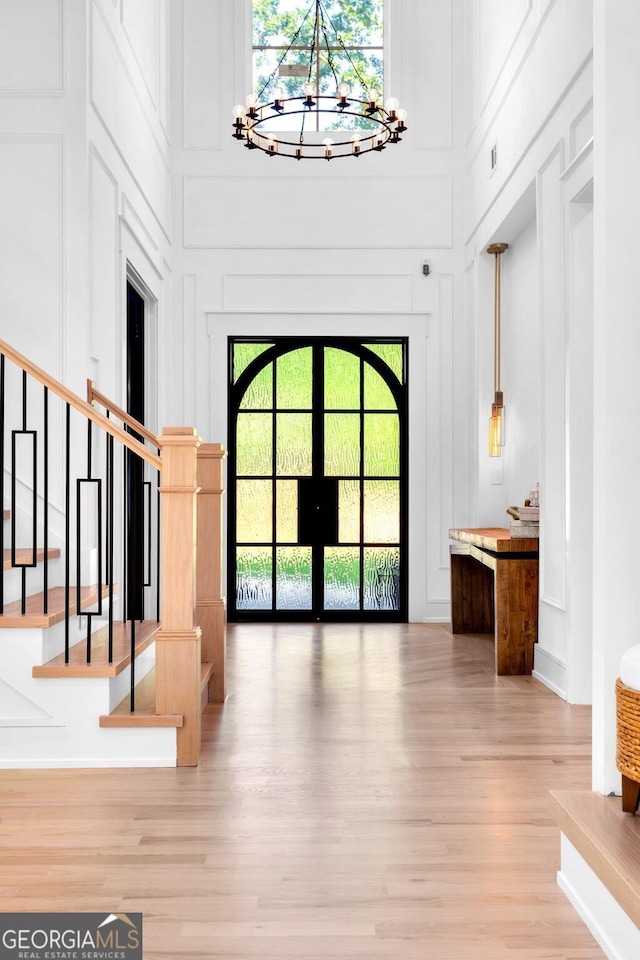 foyer entrance featuring light hardwood / wood-style floors, an inviting chandelier, a high ceiling, and french doors