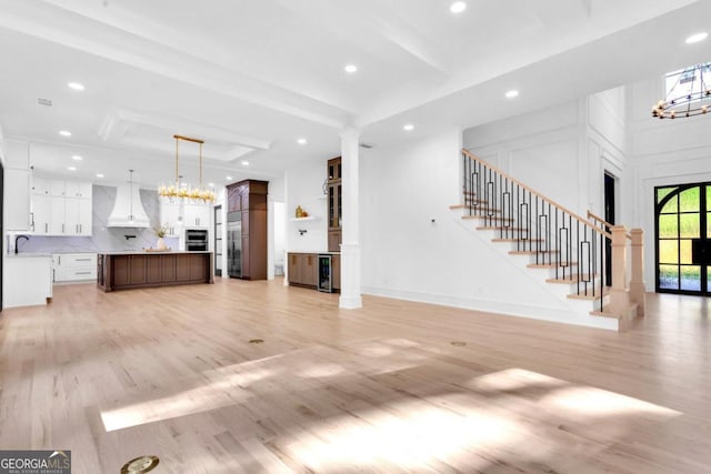 unfurnished living room featuring beam ceiling, sink, beverage cooler, and light hardwood / wood-style flooring