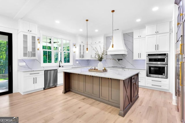 kitchen with pendant lighting, premium range hood, white cabinets, light hardwood / wood-style flooring, and a large island