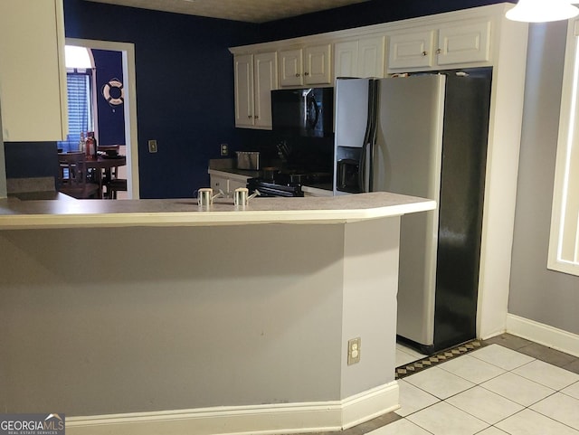 kitchen with light tile flooring, stainless steel refrigerator with ice dispenser, white cabinetry, and stove