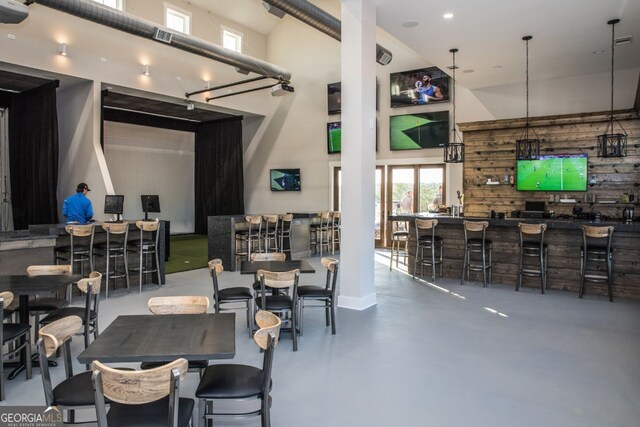 dining room featuring bar area, concrete flooring, and a towering ceiling