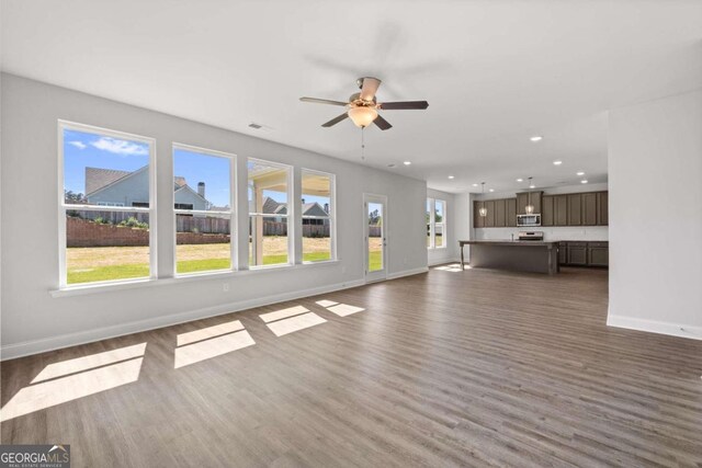 unfurnished living room featuring ceiling fan, a healthy amount of sunlight, and dark hardwood / wood-style flooring