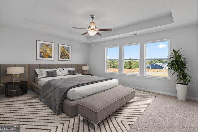 carpeted bedroom featuring a tray ceiling and ceiling fan