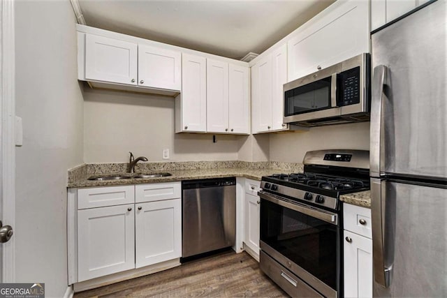 kitchen featuring dark hardwood / wood-style flooring, stainless steel appliances, sink, dark stone countertops, and white cabinetry