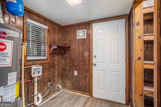 laundry room featuring hookup for a washing machine, gas water heater, electric dryer hookup, wooden walls, and hardwood / wood-style floors