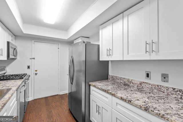 kitchen with dark hardwood / wood-style flooring, light stone counters, stainless steel appliances, a raised ceiling, and white cabinets