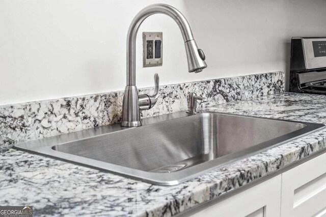 details with light stone countertops, white cabinetry, and sink