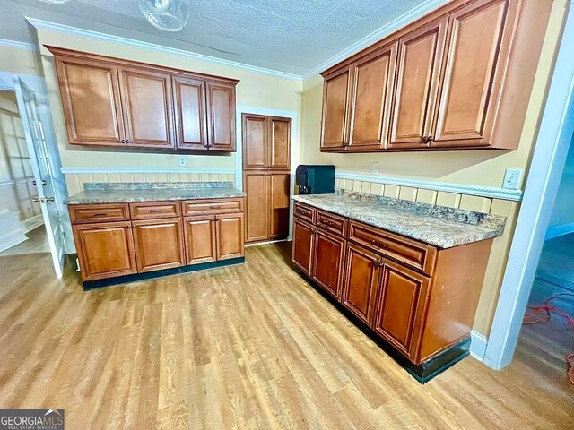 kitchen featuring light stone counters, ornamental molding, and light wood-type flooring