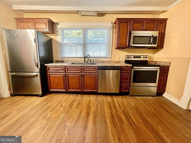 kitchen featuring stainless steel appliances, ornamental molding, sink, light wood-type flooring, and light stone countertops