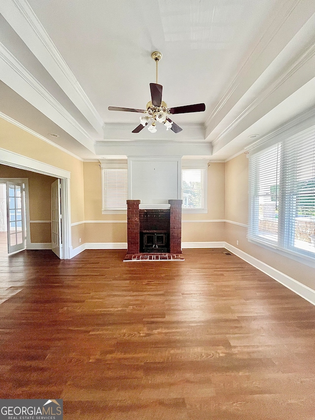 unfurnished living room with wood-type flooring, ornamental molding, a tray ceiling, and a fireplace