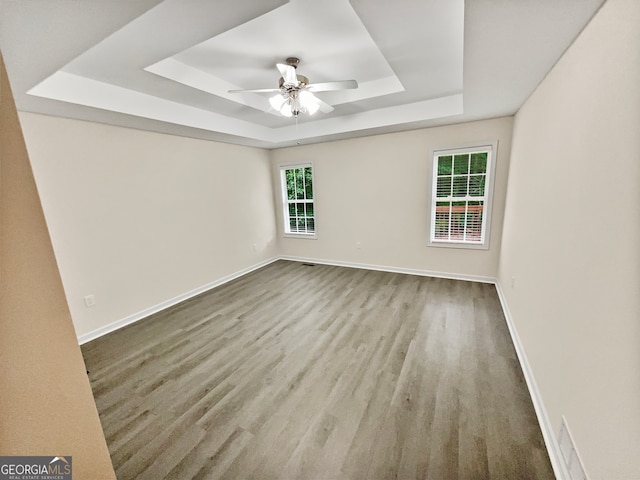 empty room featuring ceiling fan, a healthy amount of sunlight, light wood-type flooring, and a tray ceiling