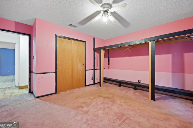 unfurnished bedroom featuring light carpet, a textured ceiling, and ceiling fan