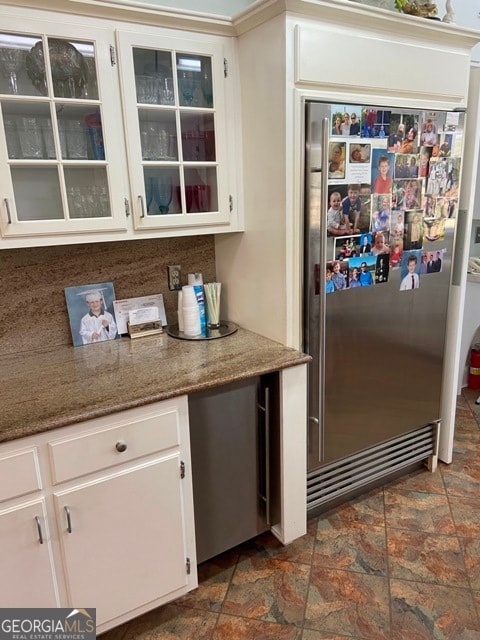 kitchen featuring light stone countertops, high end refrigerator, tasteful backsplash, and white cabinetry