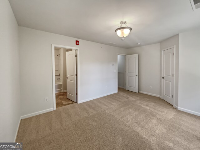 unfurnished bedroom with light colored carpet and connected bathroom