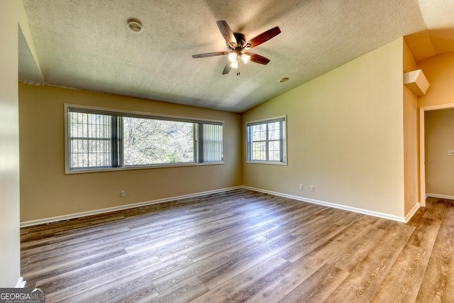 empty room with ceiling fan, vaulted ceiling, a textured ceiling, and wood-type flooring