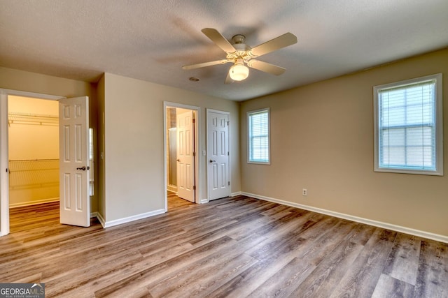 unfurnished bedroom with hardwood / wood-style flooring, multiple windows, a textured ceiling, and ceiling fan