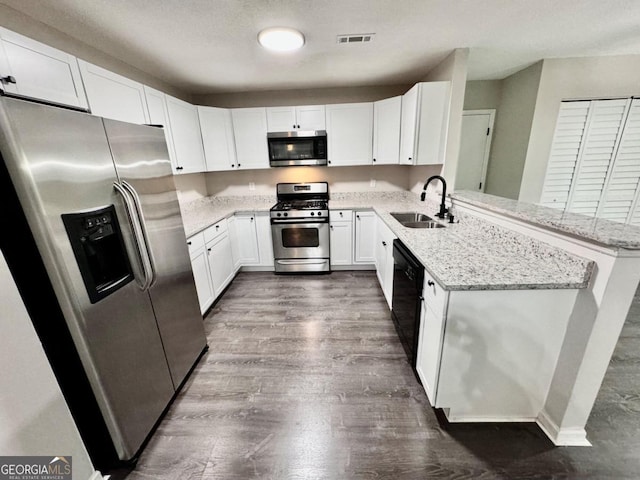 kitchen featuring white cabinetry, kitchen peninsula, appliances with stainless steel finishes, light stone counters, and sink