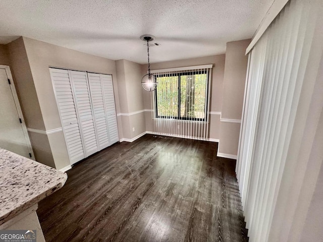 unfurnished dining area featuring a textured ceiling and dark hardwood / wood-style flooring