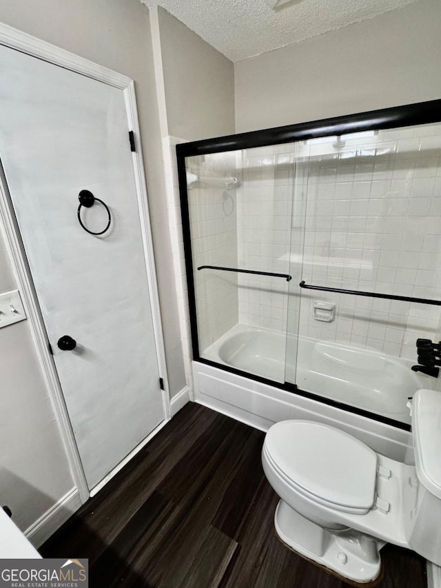 bathroom featuring a textured ceiling, enclosed tub / shower combo, toilet, and hardwood / wood-style floors