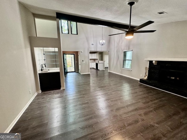 unfurnished living room with ceiling fan, dark hardwood / wood-style flooring, a towering ceiling, and a textured ceiling