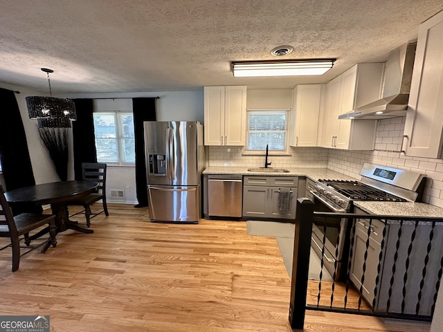 kitchen featuring light hardwood / wood-style floors, appliances with stainless steel finishes, wall chimney exhaust hood, and white cabinets