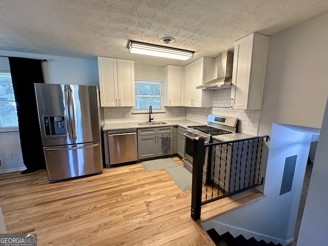 kitchen featuring light hardwood / wood-style flooring, appliances with stainless steel finishes, sink, white cabinetry, and wall chimney range hood