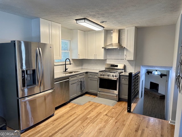 kitchen featuring wall chimney exhaust hood, light hardwood / wood-style flooring, stainless steel appliances, sink, and gray cabinets