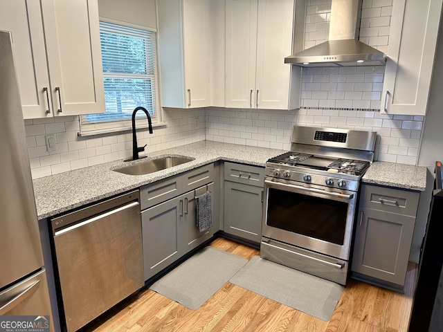 kitchen with light wood-type flooring, light stone counters, sink, wall chimney exhaust hood, and appliances with stainless steel finishes